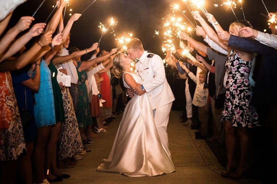 bride and groom kissing at night while wedding guests hold sparklers on either side of pathway